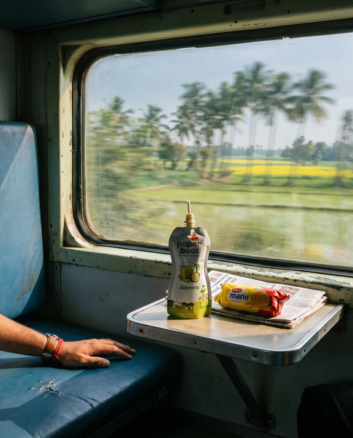 A Paper Boat Jaljeera pouch on a train tray table, green fields blurring past the window